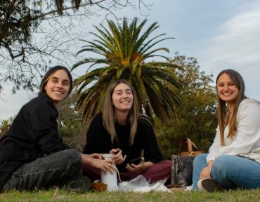 Three young adults enjoy a picnic outdoors, creating a joyful and relaxed atmosphere.